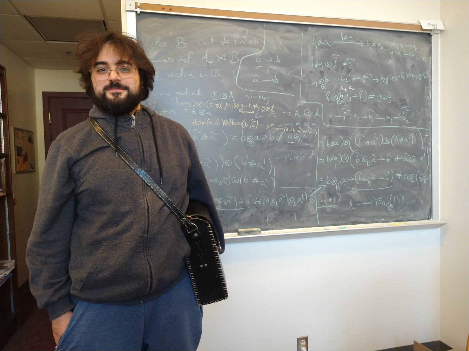 Héctor Martín Peña Pollastri standing beside a chalkboard filled with mathematics
